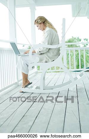 Woman sitting in rocking chair on porch, using laptop computer, full length View Large Photo Image Stock Photograph - Woman sitting in rocking chair on porch, using laptop computer, full length. Fotosearch