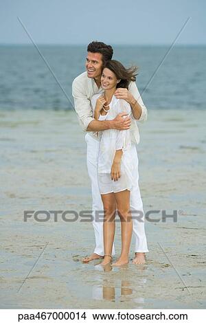 Picture - Man and teen girl on beach, standing together, looking at view, full length. Fotosearch