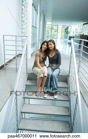 Stock Image - Mother and teenage girl together, sitting on steps, smiling at camera, full length. Fotosearch