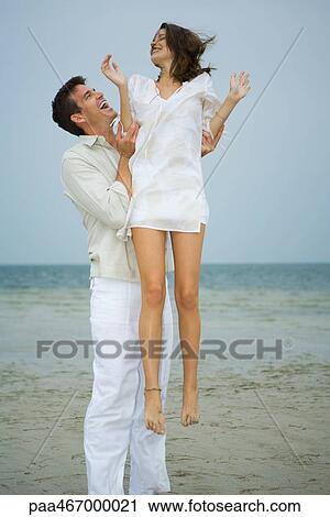On beach, man holding young female companion up in air, full length View Large Photo Image Stock Image - On beach, man holding young female companion up in air, full length. Fotosearch