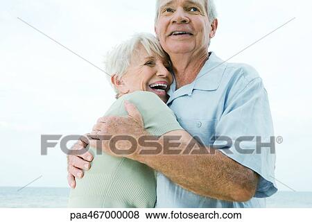 Stock Photo - Senior couple hugging, woman laughing, low angle view. Fotosearch