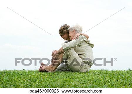 Stock Photograph - Senior woman and grandson, sitting on grass, full length. Fotosearch