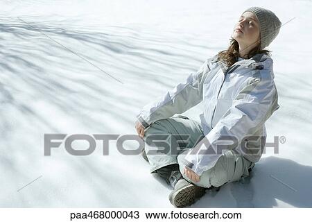 Stock Image - Teen girl sitting on snow, meditating. Fotosearch