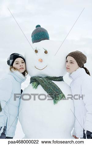 Stock Image - Two teen girls leaning against snowman. Fotosearch