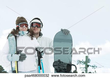 Young couple dressed in ski wear, man holding snowboard, woman holding ski sticks View Large Photo Image Stock Image - Young couple dressed in ski wear, man holding snowboard, woman holding ski sticks. Fotosearch