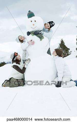 Picture - Young female friends grouped around snowman. Fotosearch