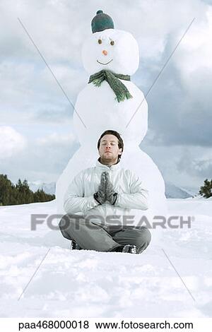 Young man meditating in front of snowman View Large Photo Image Stock Photo - Young man meditating in front of snowman. Fotosearch