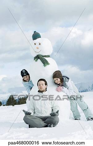Young man meditating in front of snowman, two girls creeping up behind him View Large Photo Image Stock Photograph - Young man meditating in front of snowman, two girls creeping up behind him. Fotosearch