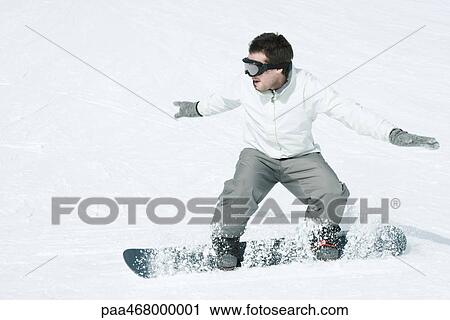 Stock Image - Young man snowboarding, action shot, full length. Fotosearch