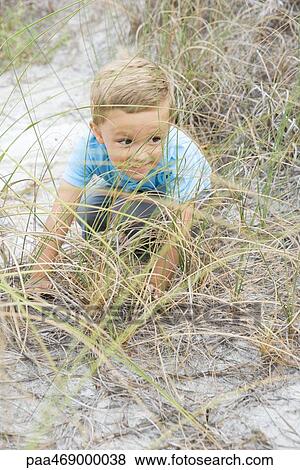 Boy crouching in dune grass, looking away mischievously, full length, high angle view View Large Photo Image Stock Photo - Boy crouching in dune grass, looking away mischievously, full length, high angle view. Fotosearch