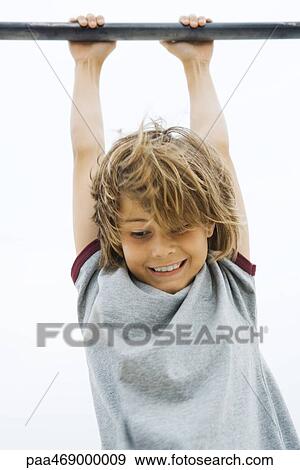 Stock Photo - Boy hanging from bar, looking down, smiling, waist up. Fotosearch