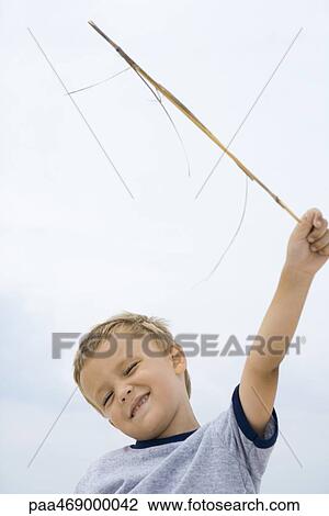 Boy holding up stick, smiling, squinting eyes closed, low angle view View Large Photo Image Stock Image - Boy holding up stick, smiling, squinting eyes closed, low angle view. Fotosearch