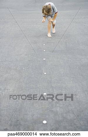 Picture - Boy placing trail of pebbles on asphalt. Fotosearch