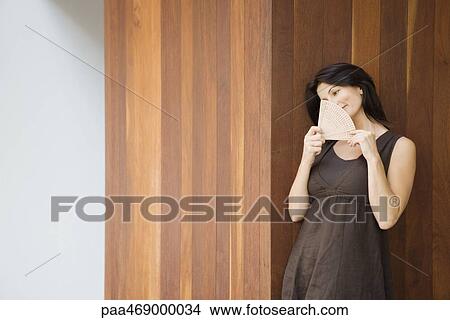 Brunette woman holding up fan in front of face, smiling, looking away View Large Photo Image Picture - Brunette woman holding up fan in front of face, smiling, looking away. Fotosearch