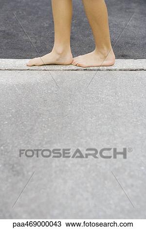 Stock Image - Child standing on edge of concrete, cropped view of calves and bare feet, side view. Fotosearch