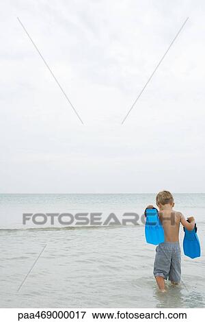 Little boy walking in shallow water, holding up flippers, rear view View Large Photo Image Stock Photo - Little boy walking in shallow water, holding up flippers, rear view. Fotosearch
