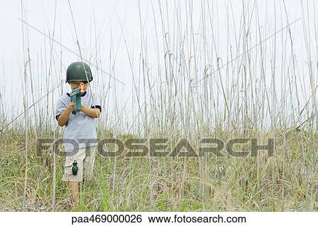 Little boy wearing toy helmet and grenade, pointing toy machine gun at camera, standing in tall grass View Large Photo Image Stock Photograph - Little boy wearing toy helmet and grenade, pointing toy machine gun at camera, standing in tall grass. Fotosearch
