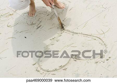 Man tracing heart in sand with stick, high angle view, cropped view View Large Photo Image Stock Photo - Man tracing heart in sand with stick, high angle view, cropped view. Fotosearch