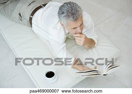 Mature man lying on stomach on chaise longue, reading book, cup of coffee nearby, high angle view View Large Photo Image Stock Photo - Mature man lying on stomach on chaise longue, reading book, cup of coffee nearby, high angle view. Fotosearch