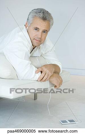 Mature man lying on stomach on chaise longue, listening to MP3 player, looking at camera View Large Photo Image Stock Photography - Mature man lying on stomach on chaise longue, listening to MP3 player, looking at camera. Fotosearch