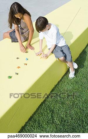 Mother and boy sitting outdoors, playing with plastic animal figurines, high angle view, full length View Large Photo Image Picture - Mother and boy sitting outdoors, playing with plastic animal figurines, high angle view, full length. Fotosearch