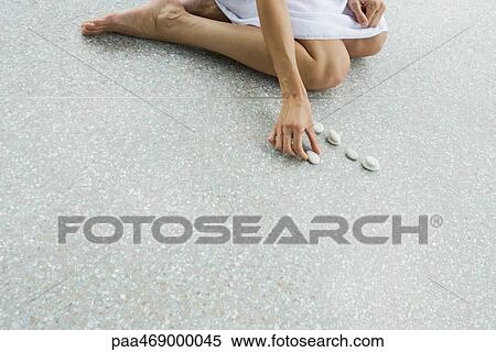 Stock Photography - Woman kneeling on floor, placing pebbles in line, cropped, high angle view. Fotosearch