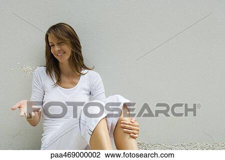Woman sitting on ground with knees up, tossing handful of gravel into air, smiling View Large Photo Image Stock Image - Woman sitting on ground with knees up, tossing handful of gravel into air, smiling. Fotosearch