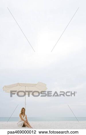 Woman wearing sundress, sitting under parasol on beach, full length View Large Photo Image Stock Image - Woman wearing sundress, sitting under parasol on beach, full length. Fotosearch
