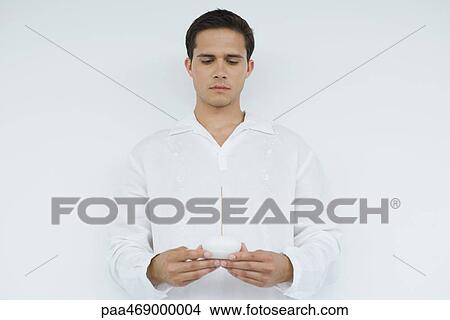 Young man dressed in white holding incense holder, looking down, waist up, front view View Large Photo Image Picture - Young man dressed in white holding incense holder, looking down, waist up, front view. Fotosearch