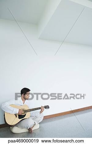 Young man sitting on floor, playing guitar, full length View Large Photo Image Stock Photo - Young man sitting on floor, playing guitar, full length. Fotosearch