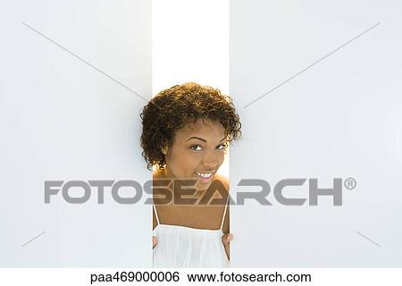 Young woman peeking through opening in walls, smiling at camera, portrait View Large Photo Image Stock Photograph - Young woman peeking through opening in walls, smiling at camera, portrait. Fotosearch