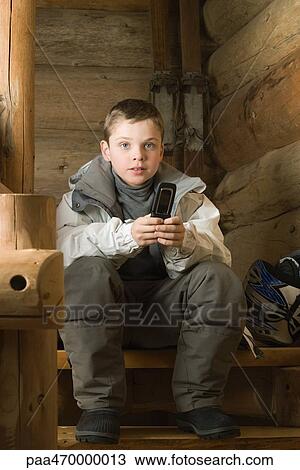 Stock Image - Boy dressed in ski clothes holding cell phone. Fotosearch