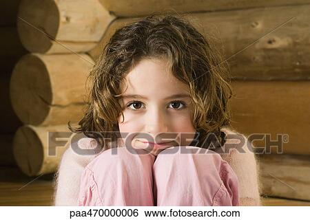 Stock Photograph - Girl sitting with head resting on knees, smiling at camera. Fotosearch