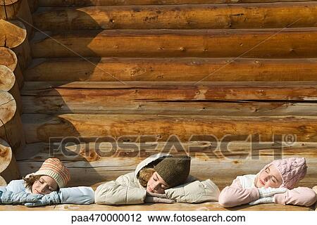 Stock Image - Three preteen or teen girls standing on deck of log cabin, resting heads on railing. Fotosearch