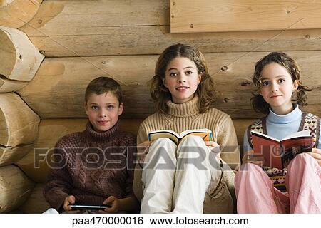 Three young siblings sitting side by side, reading and playing video game View Large Photo Image Stock Photograph - Three young siblings sitting side by side, reading and playing video game. Fotosearch