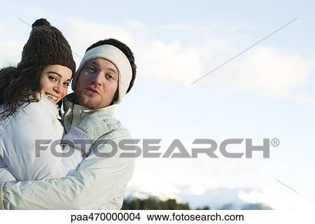 Picture - Young couple in winter clothes, embracing, smiling at camera. Fotosearch