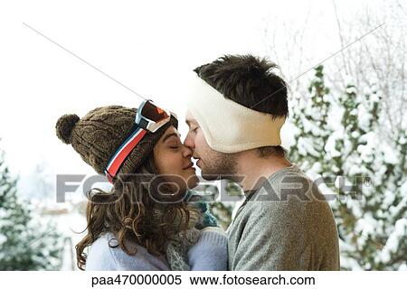 Stock Photography - Young couple in winter clothes, kissing, side view. Fotosearch
