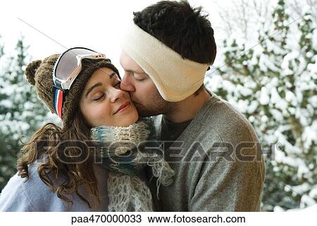 Young couple in winter clothing, man kissing woman on cheek View Large Photo Image Stock Image - Young couple in winter clothing, man kissing woman on cheek. Fotosearch