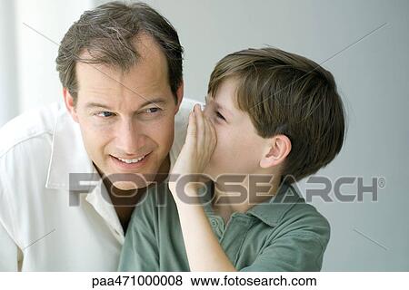 Stock Photo - Boy whispering in father's ear, close-up. Fotosearch