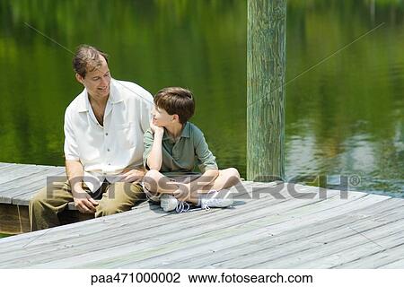 Father and son sitting on dock, smiling at each other View Large Photo Image Stock Image - Father and son sitting on dock, smiling at each other. Fotosearch