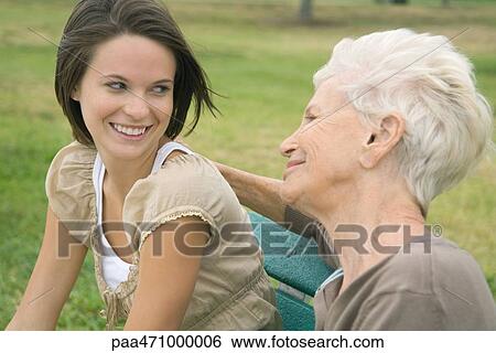 Grandmother and teenage granddaughter sitting together outdoors, smiling at each other View Large Photo Image Stock Photograph - Grandmother and teenage granddaughter sitting together outdoors, smiling at each other. Fotosearch