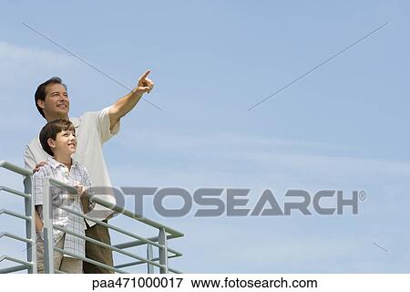 Man standing on balcony with son and pointing at sky View Large Photo Image Stock Photo - Man standing on balcony with son and pointing at sky. Fotosearch