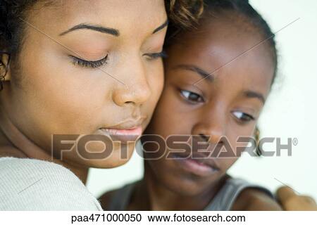Stock Image - Mother and daughter cheek to cheek, both looking down, close-up. Fotosearch