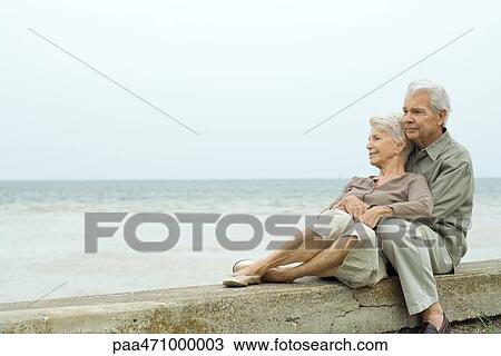 Senior couple sitting together at the beach, embracing, looking at view View Large Photo Image Stock Image - Senior couple sitting together at the beach, embracing, looking at view. Fotosearch