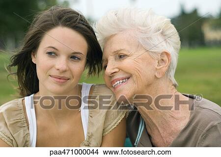Senior woman leaning head on teenage granddaughter's shoulder, both smiling and looking away View Large Photo Image Picture - Senior woman leaning head on teenage granddaughter's shoulder, both smiling and looking away. Fotosearch