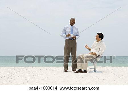 Two business associates chatting on beach, one holding coffee cup View Large Photo Image Picture - Two business associates chatting on beach, one holding coffee cup. Fotosearch