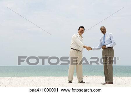 Two businessmen shaking hands on the beach, both smiling at camera View Large Photo Image Stock Image - Two businessmen shaking hands on the beach, both smiling at camera. Fotosearch
