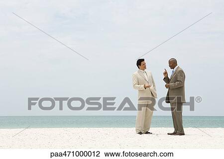 Two businessmen standing face to face at the beach having conversation View Large Photo Image Stock Image - Two businessmen standing face to face at the beach having conversation. Fotosearch