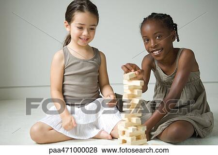 Two girls sitting on floor playing with blocks, one smiling at camera View Large Photo Image Stock Photo - Two girls sitting on floor playing with blocks, one smiling at camera. Fotosearch