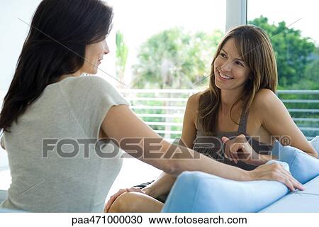 Two women sitting on couch, smiling at each other View Large Photo Image Stock Image - Two women sitting on couch, smiling at each other. Fotosearch